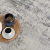 Teapot, candle, and cup on woven mat on carpet.