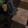 Gray blanket in wicker basket on checkered carpet.