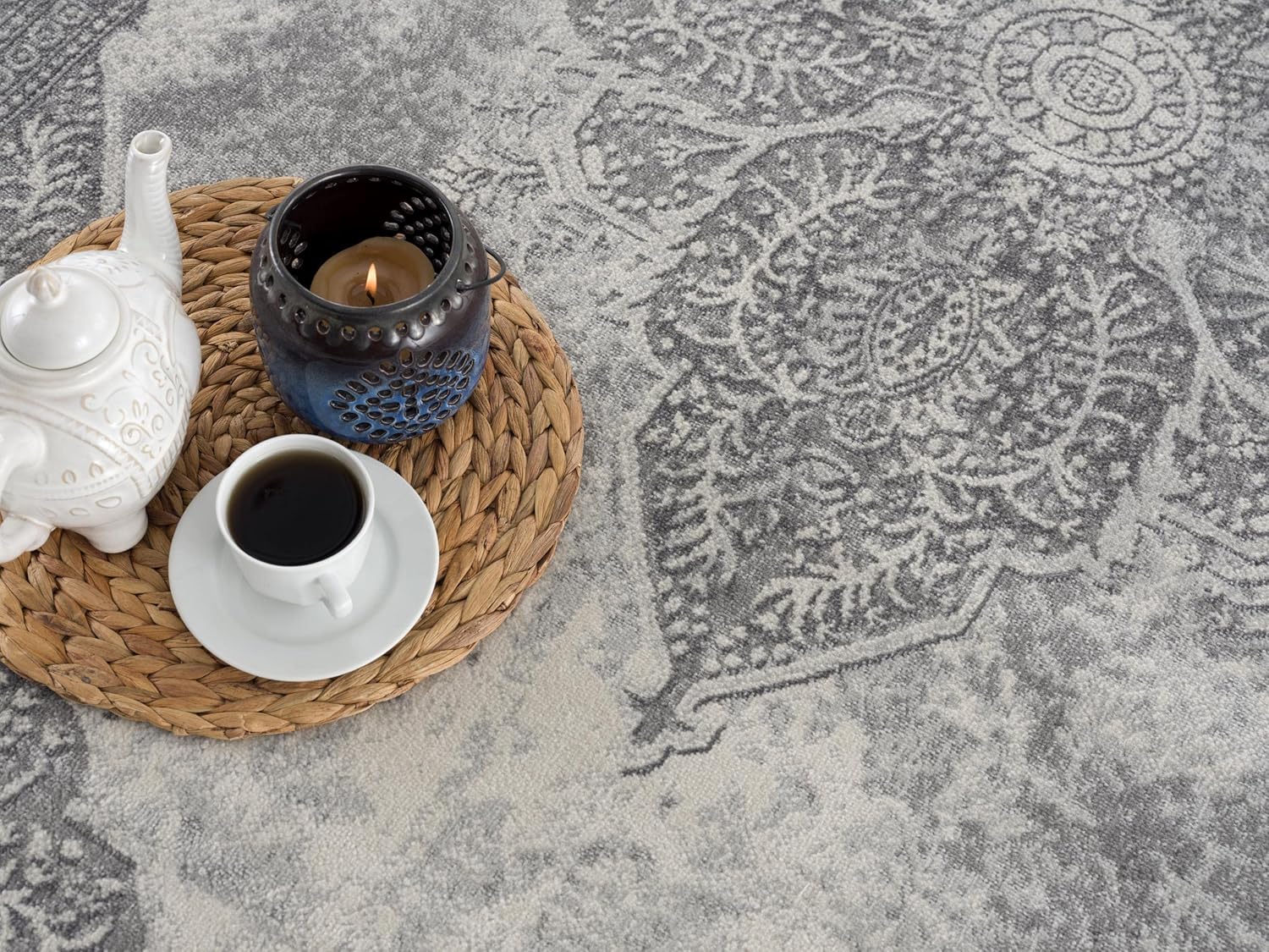 White teapot, candle, coffee on patterned rug.