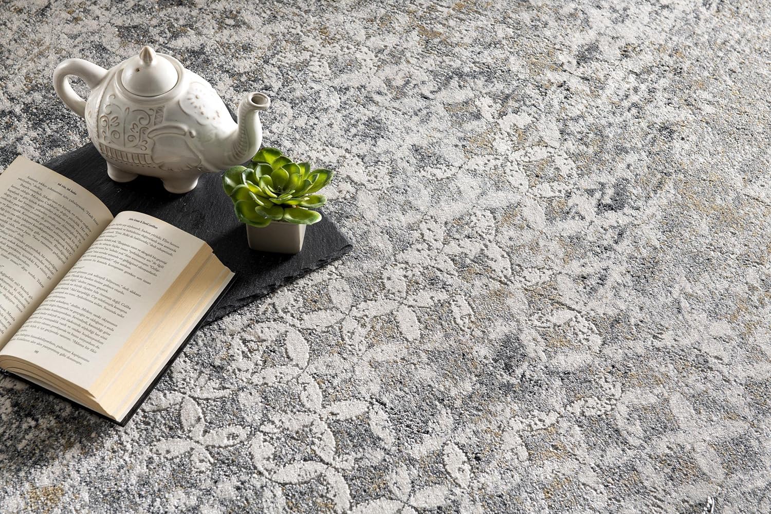 Teapot, open book, and plant on floral carpet