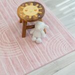 Wooden stool and plush toy on pink rug.