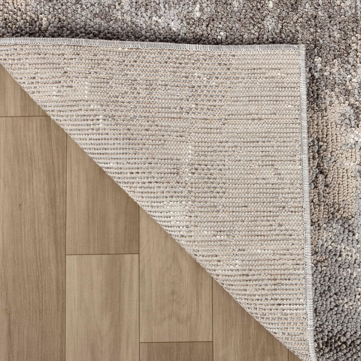 Gray shag rug on wooden floor, corner lifted.