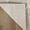 Corner of beige patterned rug on wooden floor.