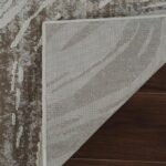 Partially flipped textured rug corner on wooden floor.