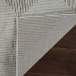 Textured gray rug corner folded on wooden floor.