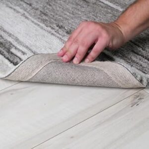 Person lifting corner of gray rug on wooden floor.