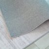 Gray rug corner folded on wooden floor.