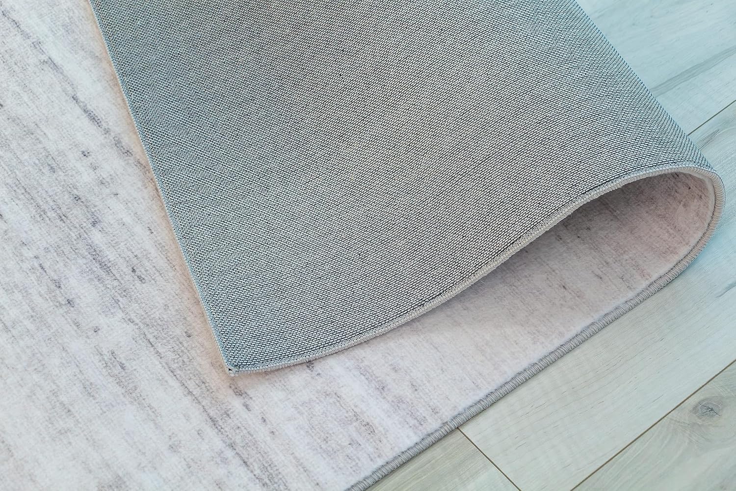 Gray rug corner folded on wooden floor.