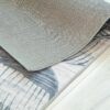 Folded gray and pattern rug on wooden floor.