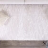 Textured white rug on wooden floor with pillows.