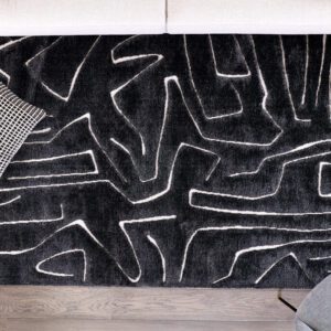 Black rug with abstract white lines on wood floor.